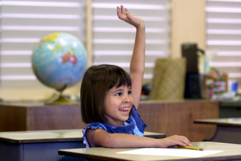 Child raising hand to ask a question in a classroom