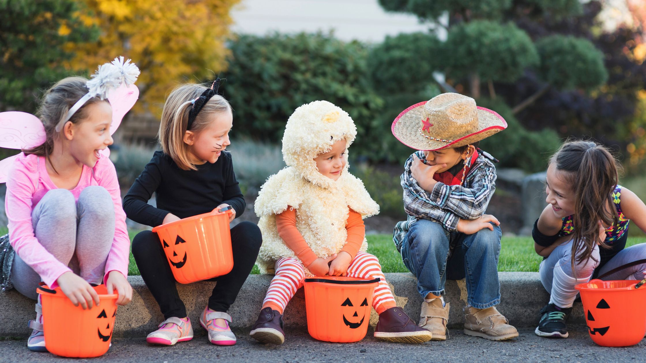5 children sitting on the curb in their Halloween costumes after trick or treating.