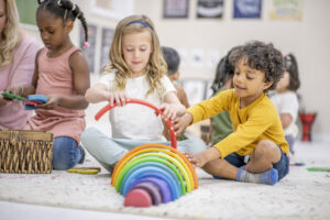 Kids playing together with colorful toys on the floor of a classroom.