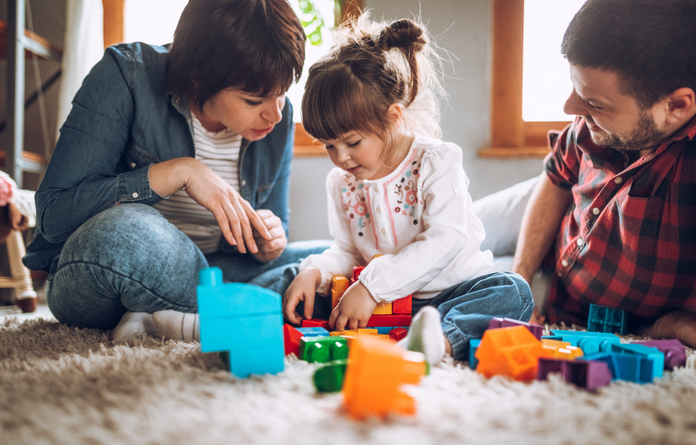 Parents and young daughter playing with blocks on the floor.