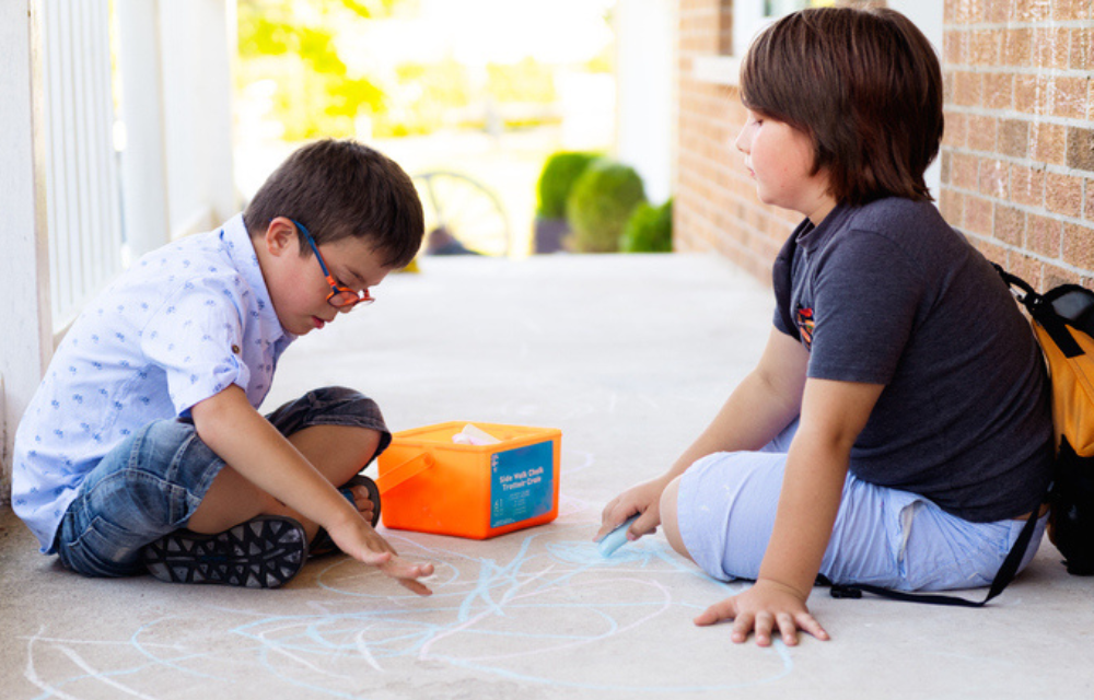 Two kids on sidewalk playing with chalk.