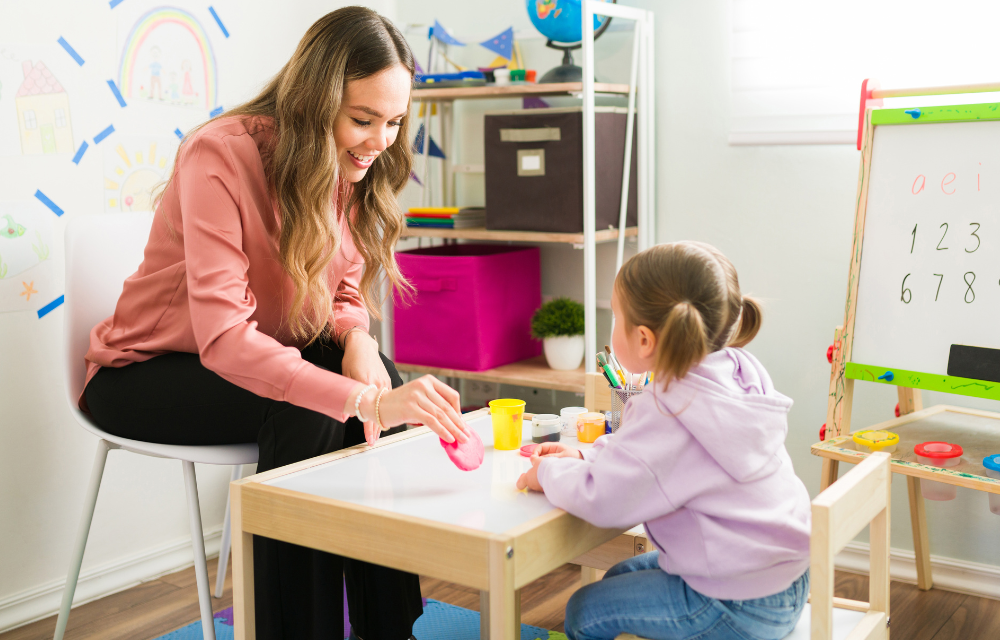 Teacher and young student playing at a classroom desk.