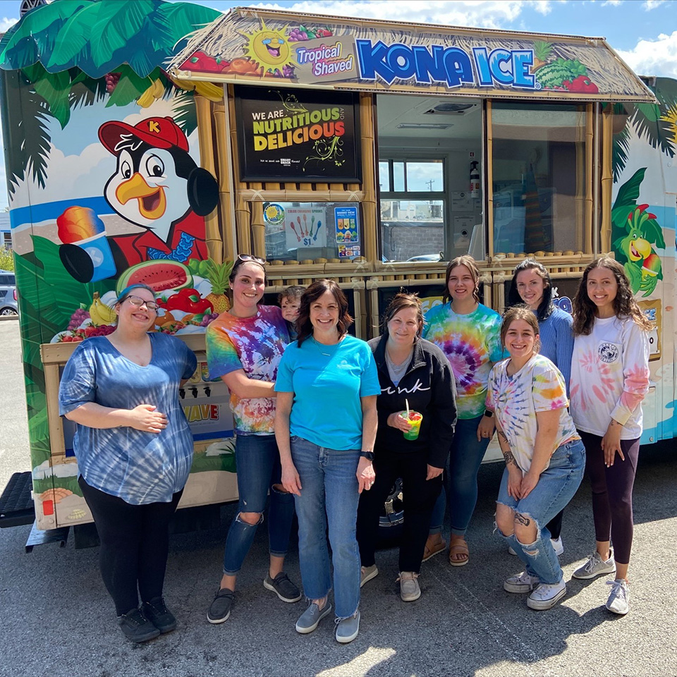 Smiling coworkers outside a kona ice cart.