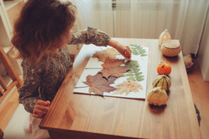 Girl placing fall leaves on paper at desk.