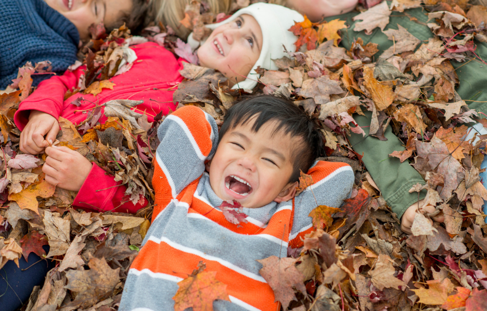 Happy kids lying on a pile of fall leaves.