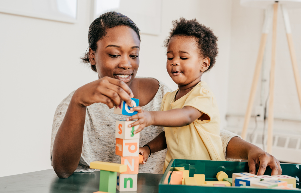 Mon and young son playing with letter blocks on a table.