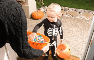 Small child in Halloween costume getting candy from bowl.