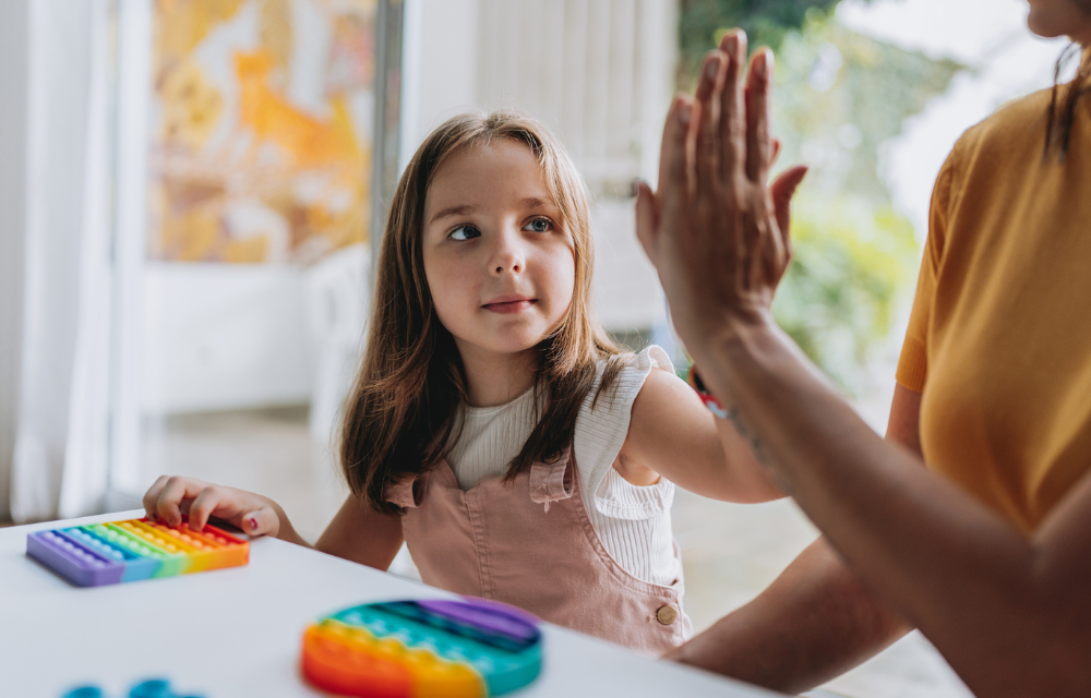 Child and adult high five while playing a game with colorful pieces at a table.