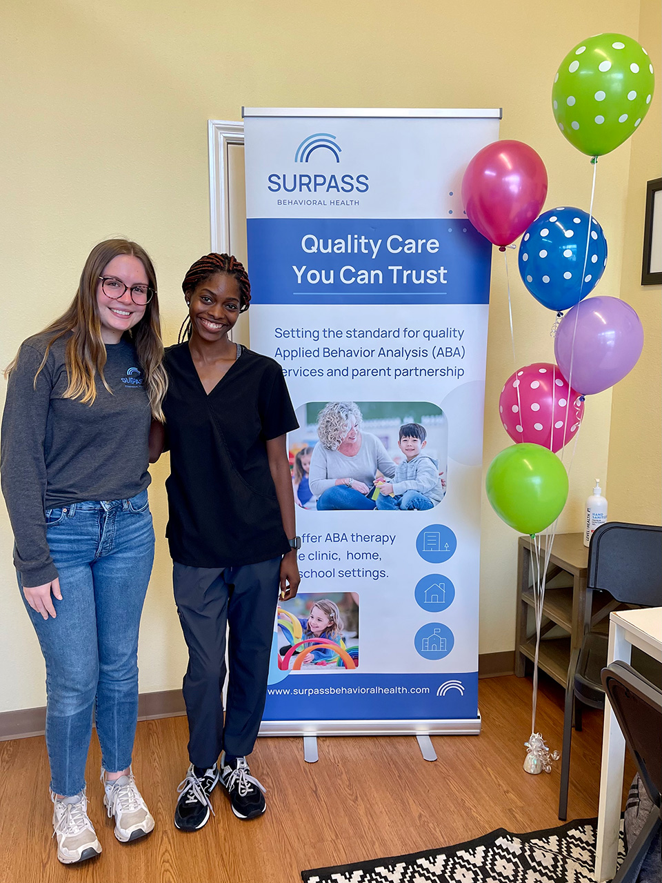 Coworkers standing next to banner and balloons.
