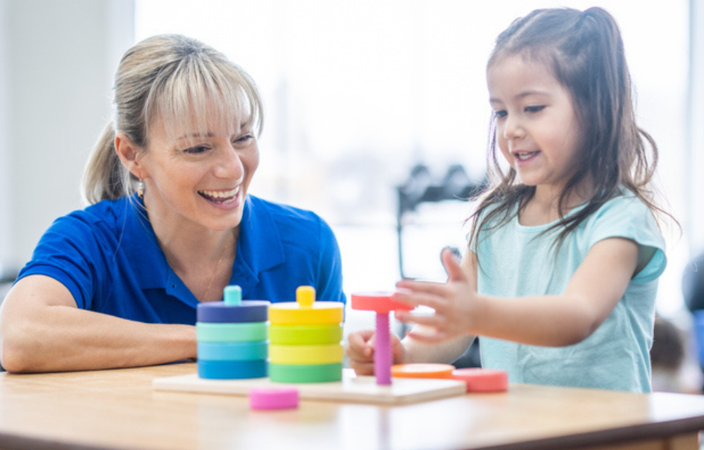 Child playing at table with colorful blocks with a teacher.