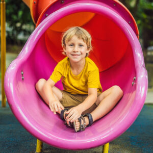 Boy sitting inside playground slide.