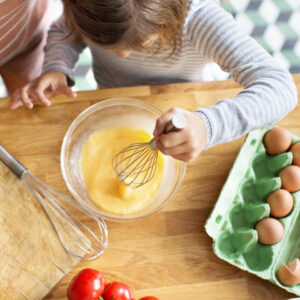 Child mixing eggs in a glass bowl on kitchen counter.