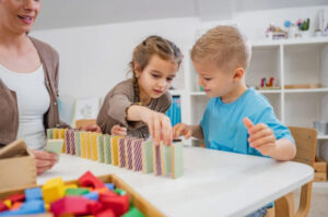 Kids play with blocks at table inside classroom.